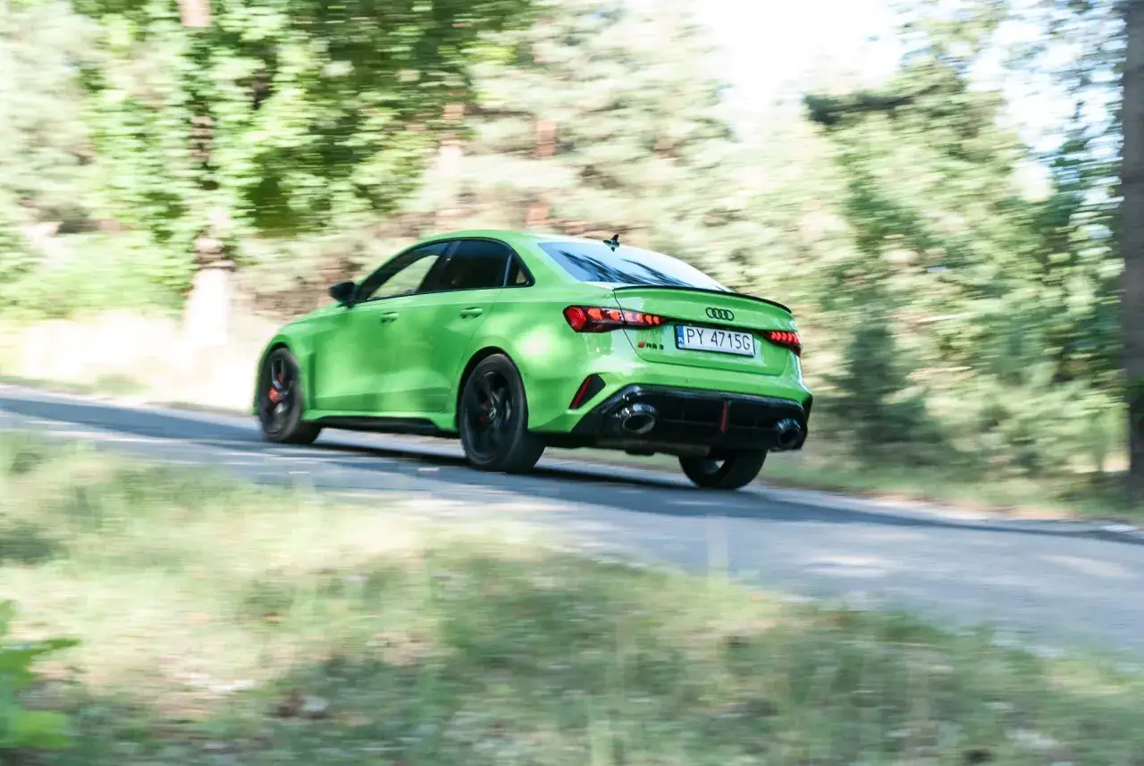 Jaskrawozielone Audi RS3 mknie po leśnej drodze, zostawiając za sobą rozmyty krajobraz.