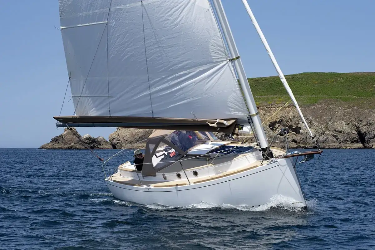 Un voilier Pabouk 700 navigue par beau temps, longeant une côte rocheuse et verdoyante.