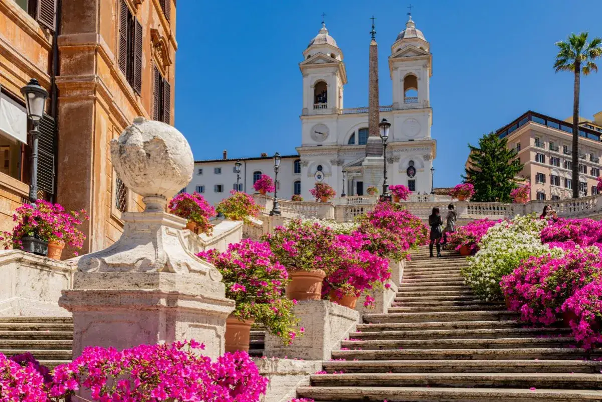 Scalinata di Trinità dei Monti a Roma, fiorita di rosa e bianca, con la chiesa sullo sfondo.