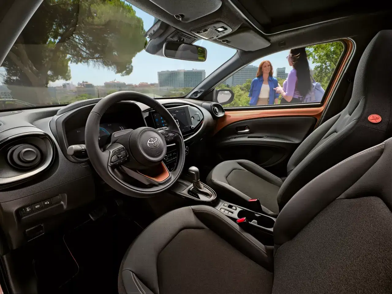 Wnętrze Toyoty Aygo X z dwoma kobietami na zewnątrz. Sprawdź atrakcyjną toyota aygo x cena.