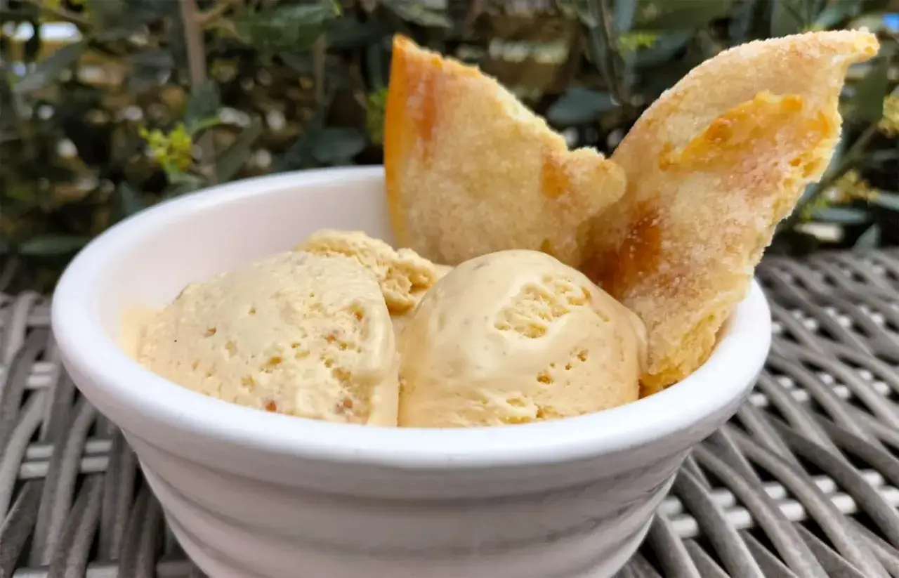 Schaufeln von cremigem Marzipan Eis in einer weißen Schale, garniert mit knusprigen Keksen.