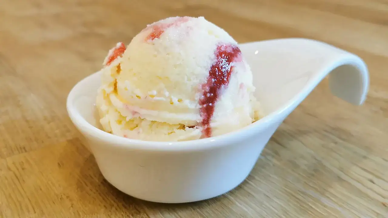 Ein cremiges Eis mit Sahne und roten Fruchtstreifen in einer wei&szlig;en Schale auf Holzhintergrund.