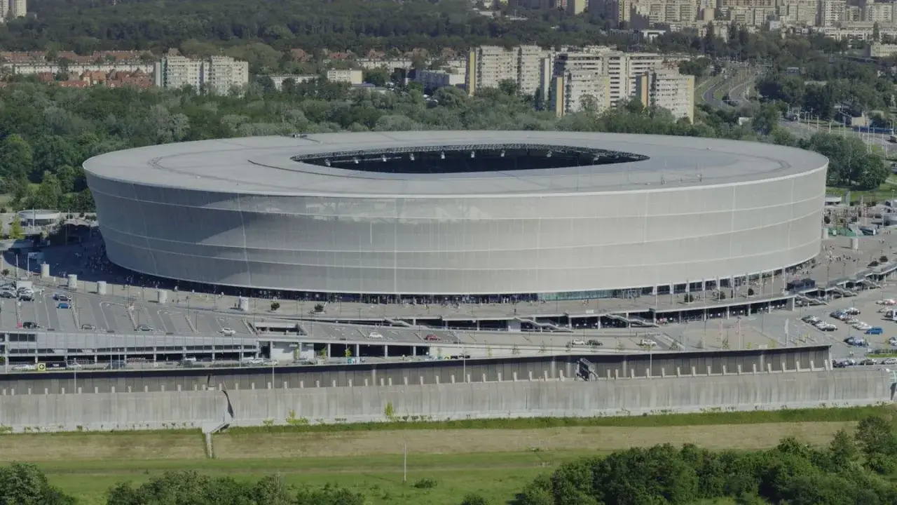 Nowoczesny stadion, jeden z największych w Polsce, z charakterystyczną, ażurową fasadą. Otoczony parkingami i zielenią.