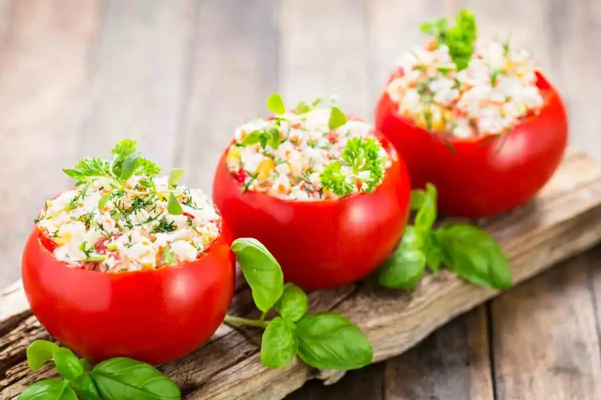 Tre pomodori ripieni freddi, farciti con un'insalata fresca e guarniti con erbe aromatiche, su un tagliere di legno.