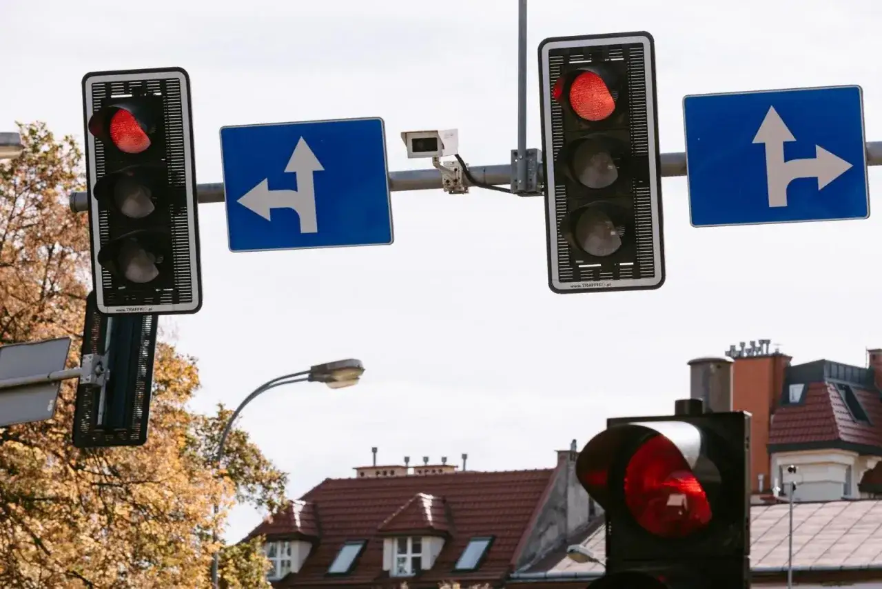 Sygnalizacja świetlna pokazuje czerwone światło, zakazując wjazdu. Znaki kierunkowe wskazują dozwolone kierunki jazdy.