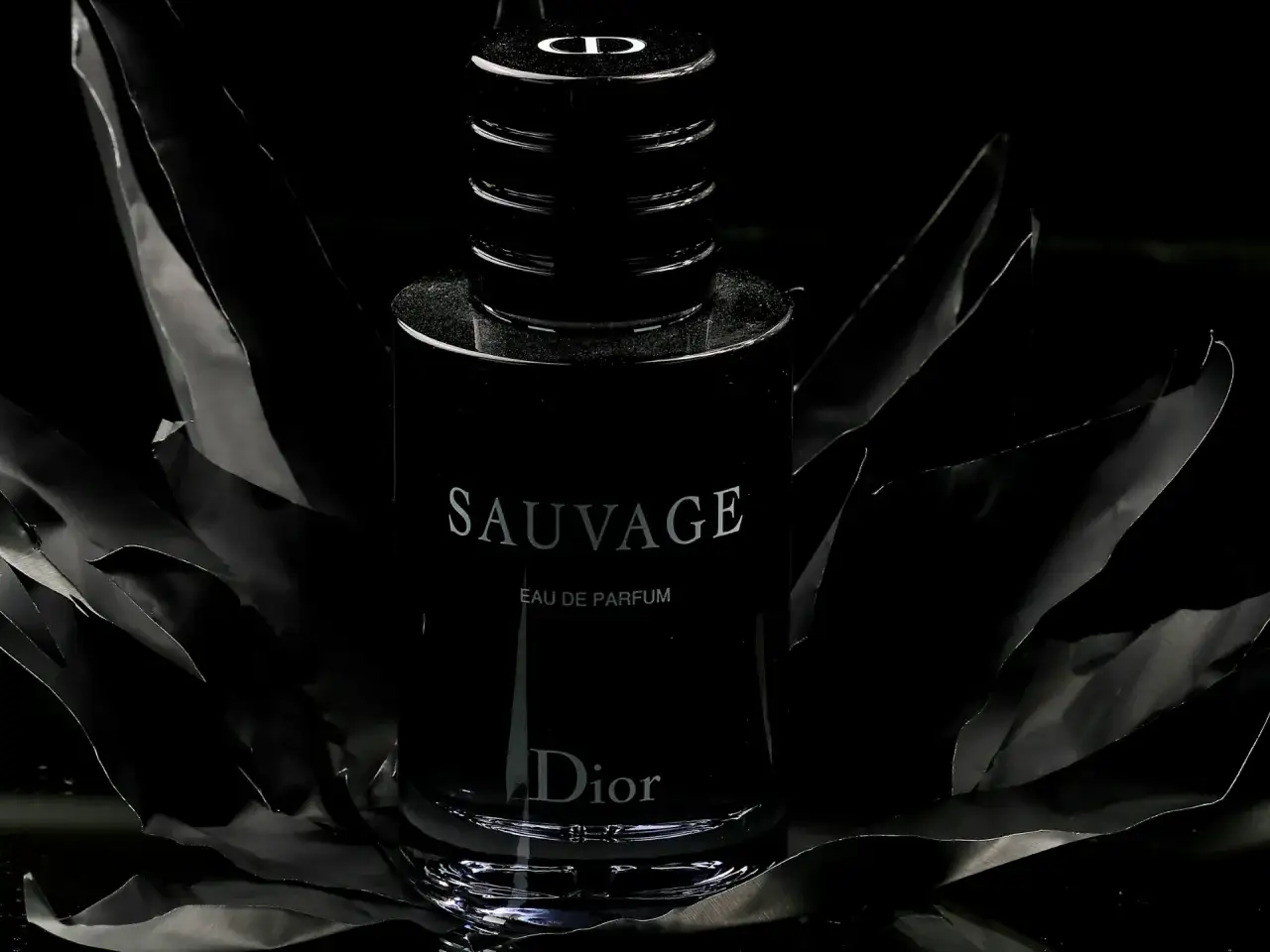 Elegancka woda perfumowana Dior Sauvage dla mężczyzn, otoczona czarnymi, falującymi płatkami.