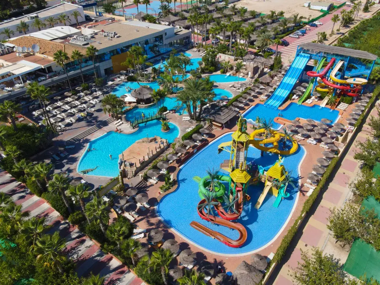 Un resort acuático con toboganes, piscinas y palmeras, ideal para campamentos para familias.