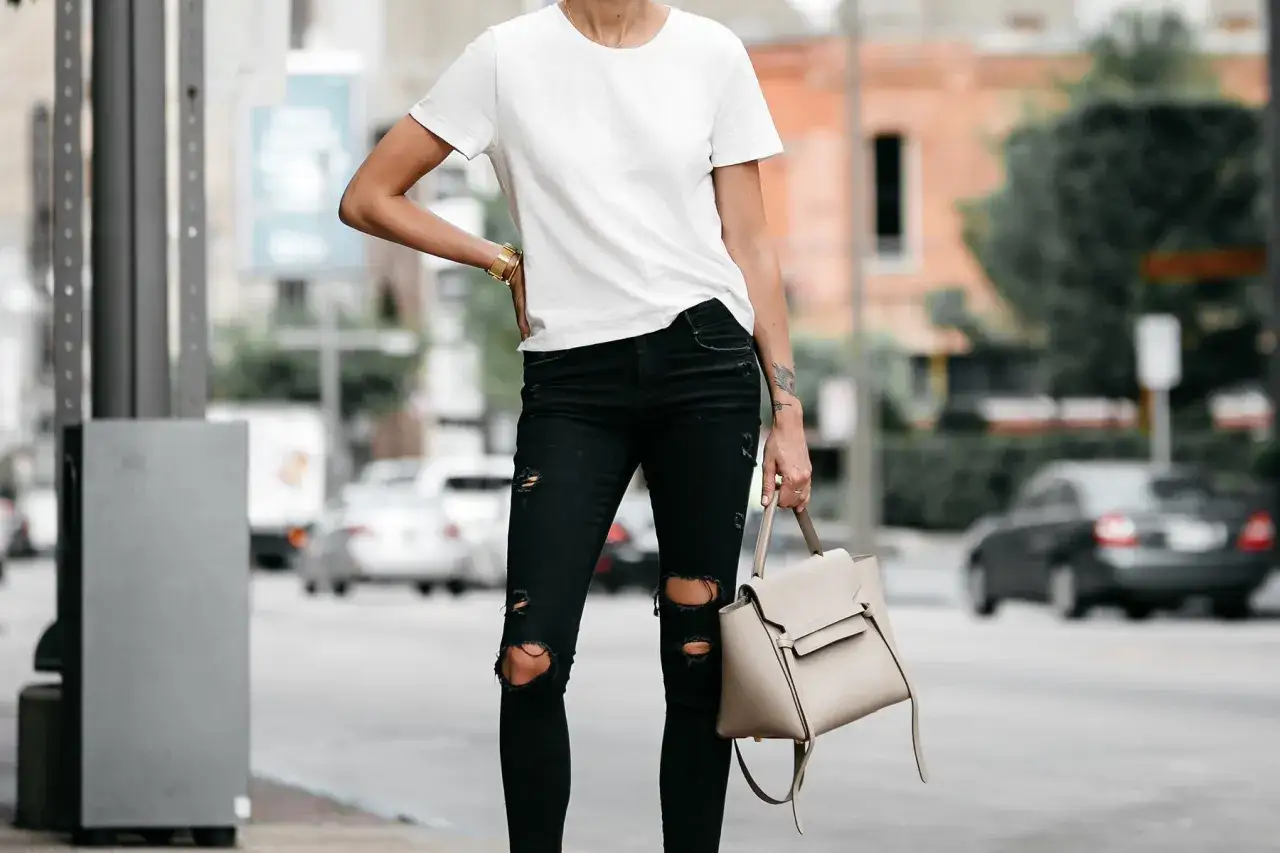 Donna con un outfit jeans e maglietta bianca, porta una borsa beige.