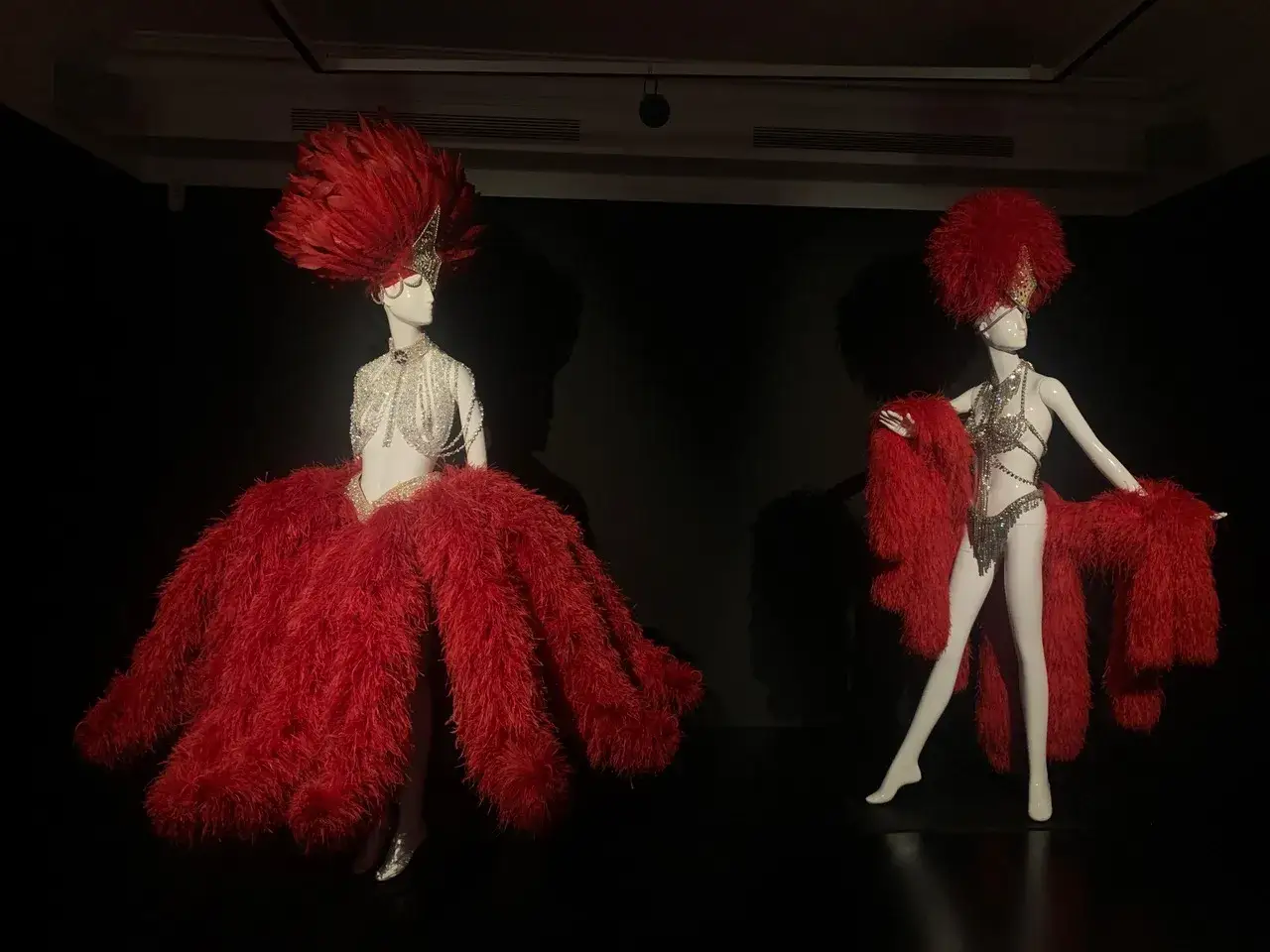 Deux mannequins portent des costumes de spectacle ornés de plumes rouges, témoignage du savoir-faire d'un artisan plumassier.