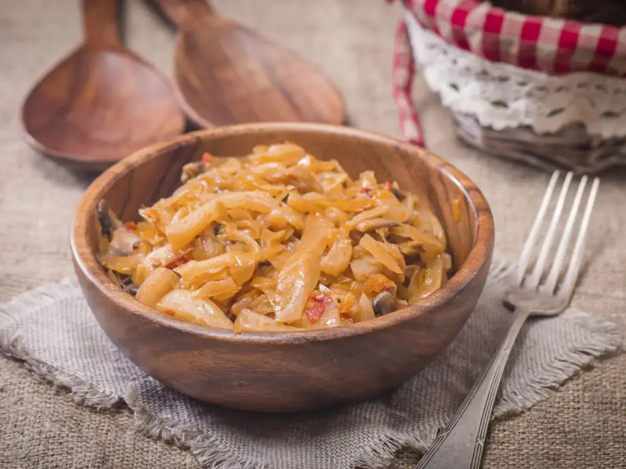 Herzhaftes Schmorkohl Rezept in einer Holzschale, serviert mit einem Löffel und einer Gabel.