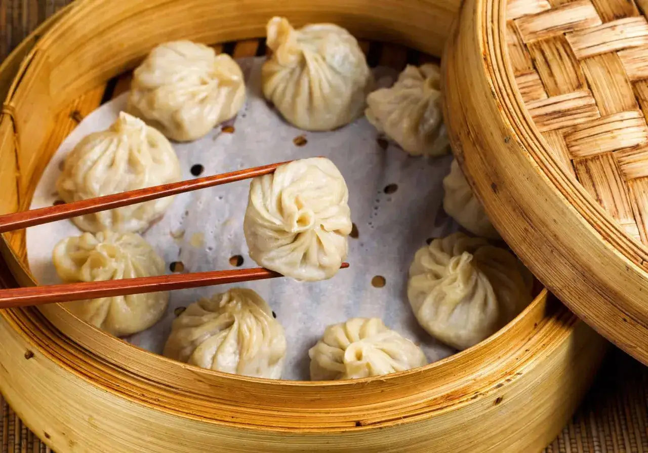 Dampfende Teigtaschen, perfekt für ein leckeres dumplings rezept, werden mit Stäbchen aus einem Bambuskorb gehoben.
