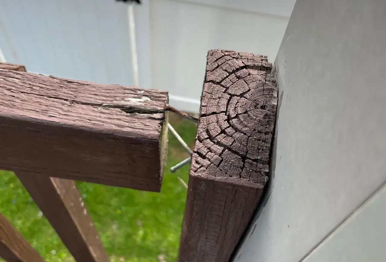 Close-up of weathered wood posts, showing cracks and peeling paint, as part of a deck railing installation.