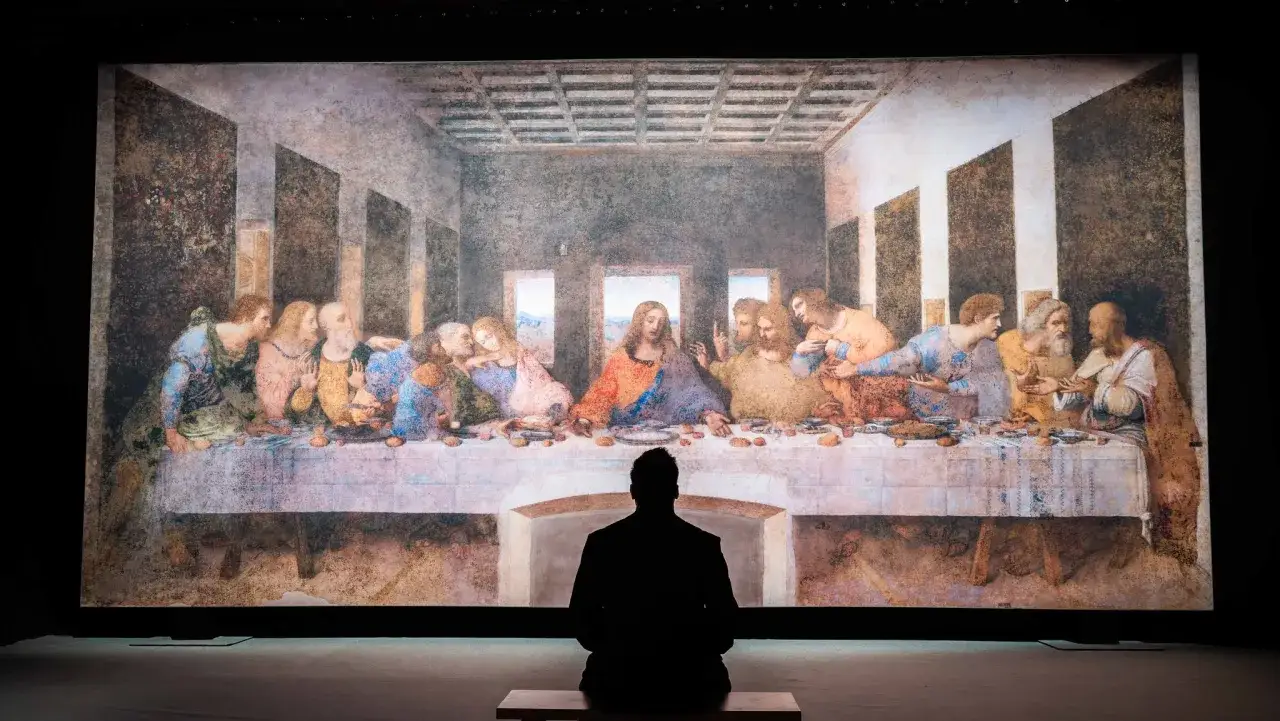 Ein Mann sitzt vor einer Projektion von das abendmahl bild original. Die Apostel sind um Jesus versammelt.