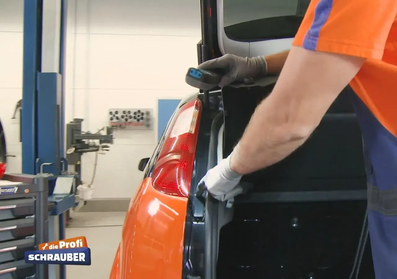 Ein Mechaniker wechselt das Bremslicht eines orangefarbenen Ford Focus.