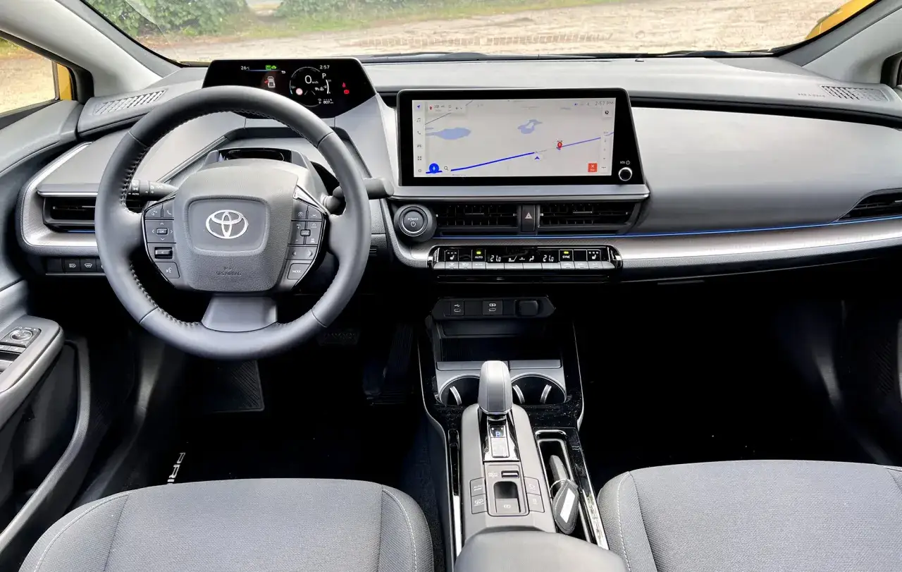 Wnętrze Toyoty Prius z ekranem nawigacji, kierownicą i panelem klimatyzacji.