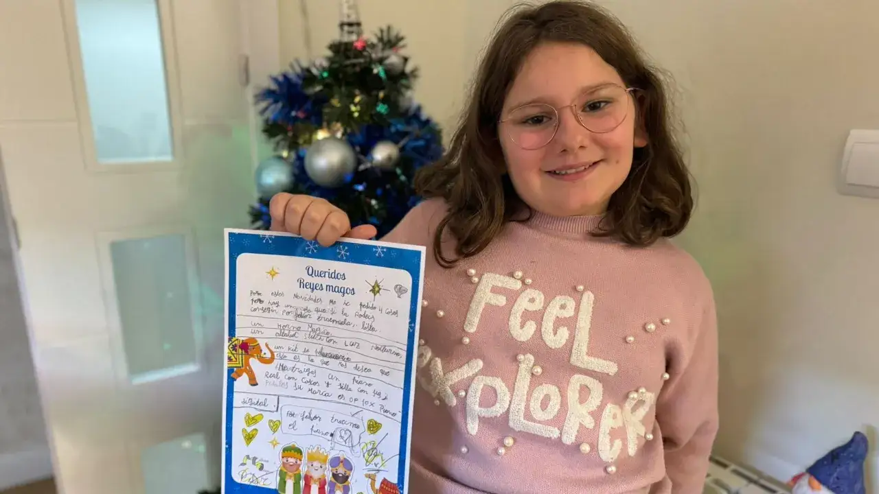 Niña sonriente muestra su carta a los Reyes Magos, pidiendo un piano y otros regalos.