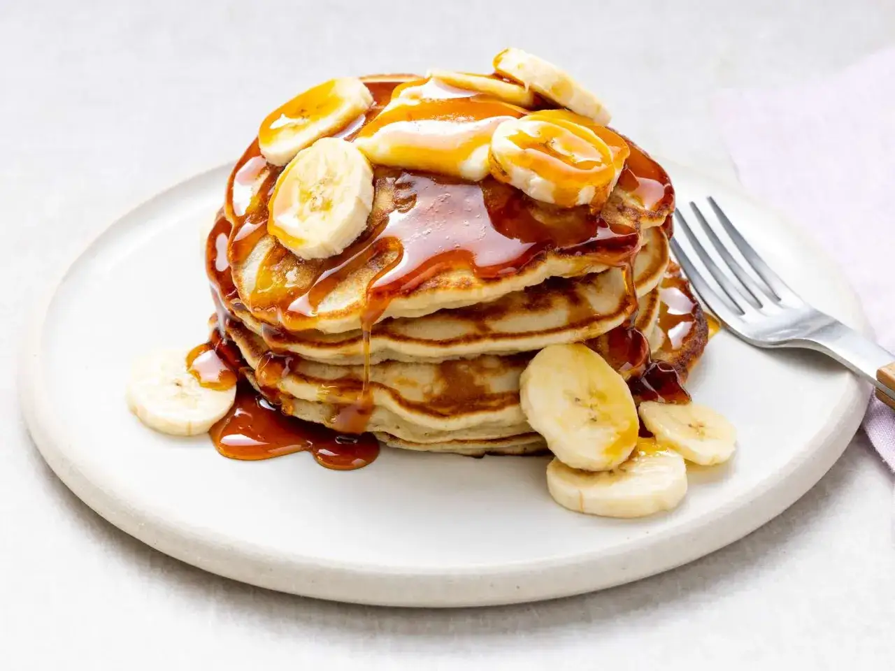 Ein Stapel goldbrauner Bananen-Pancakes, übergossen mit karamellfarbenem Sirup und garniert mit frischen Bananenscheiben.