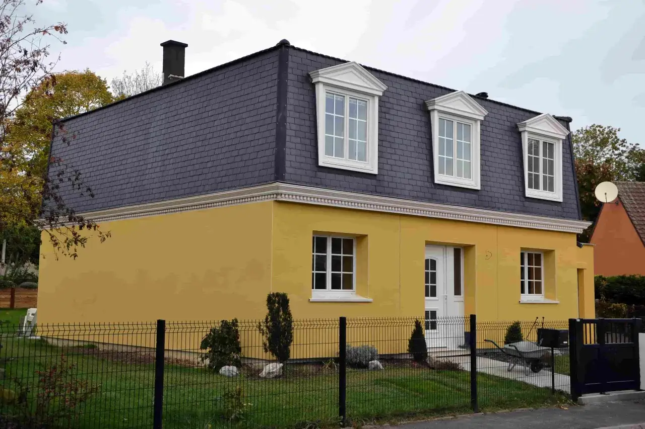 Maison moderne avec toiture en ardoise et murs jaunes vifs. L'isolation extérieur finition est soignée, avec des fenêtres blanches et une porte d'entrée élégante.