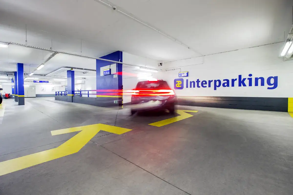 Ein Auto fährt durch ein Parkhaus mit gelben Pfeilen auf dem Boden. Die Lichter des Autos ziehen Streifen. Vielleicht geht es mit dem Auto nach Paris.