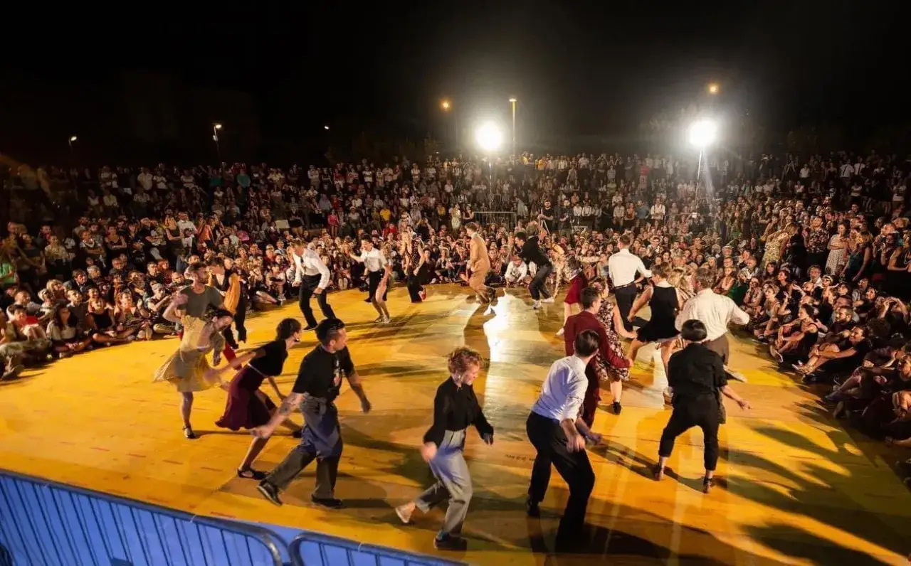 Ballerini in abiti vintage danzano al ritmo della musica swing, con un pubblico numeroso che assiste.