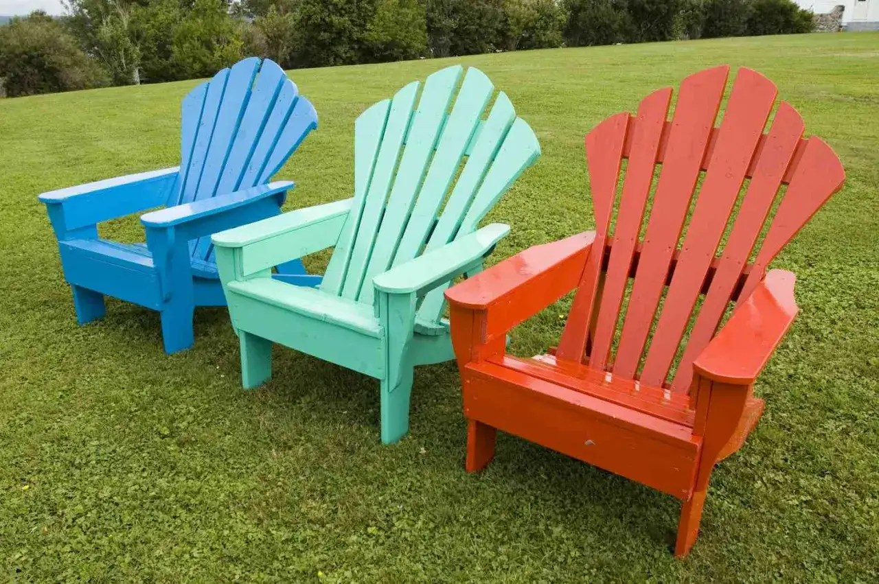 Tres sillas de madera de colores vibrantes (azul, verde menta y naranja) en el césped, listas para disfrutar del verano. ¡Pintar sillas de madera sin lijar es fácil y rápido!