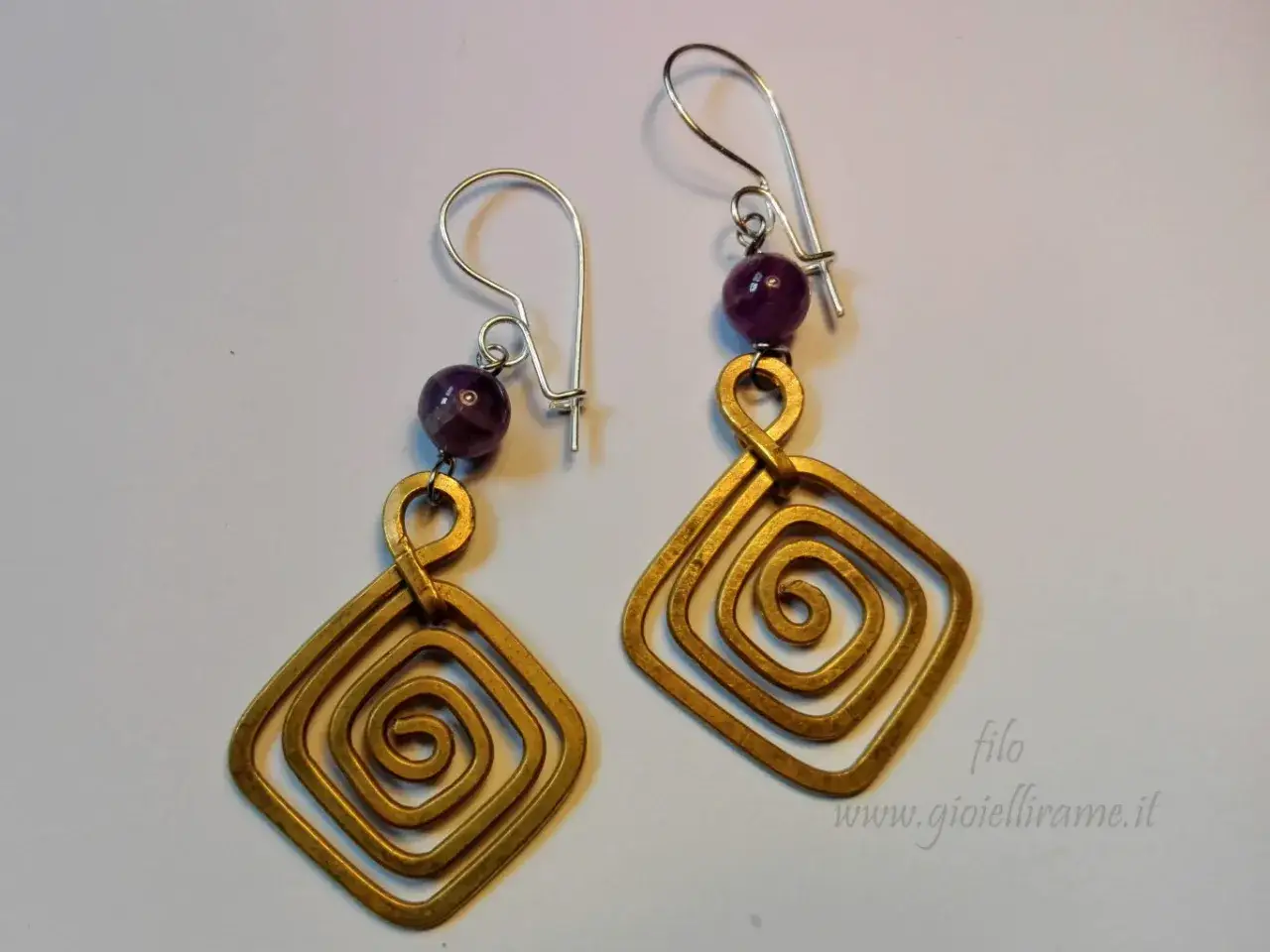 Orecchini pendenti con spirali quadrate in metallo dorato e perle di ametista, realizzati con la tecnica del wire wrapping.