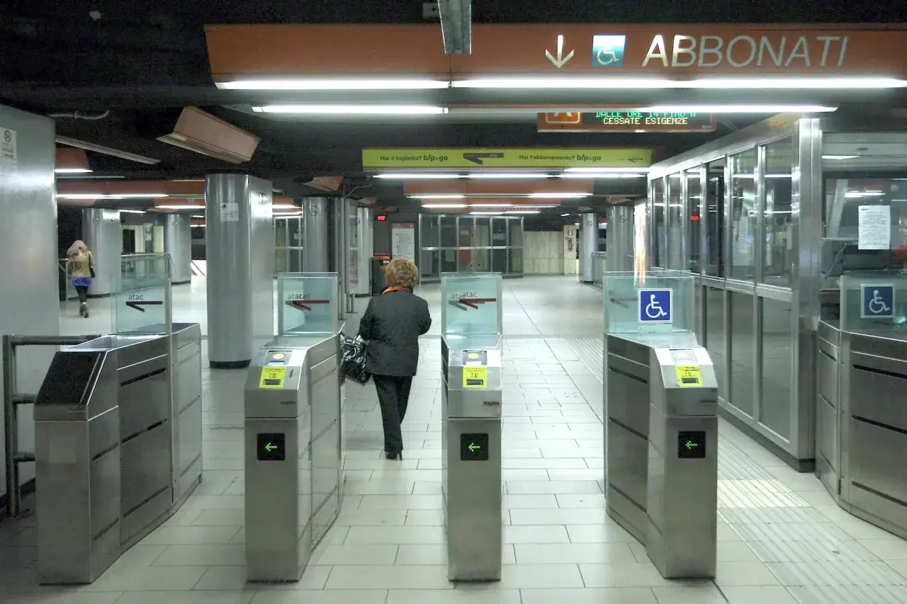 Cancelli automatici in una stazione metro. Una donna passa attraverso un tornello, mostrando che il biglietto del treno vale anche per la metro.