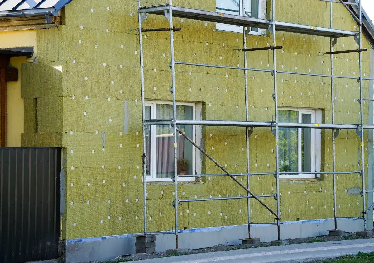 Lavori in corso per pulire muro esterno con cappotto isolante. L'edificio &egrave; circondato da ponteggi metallici.