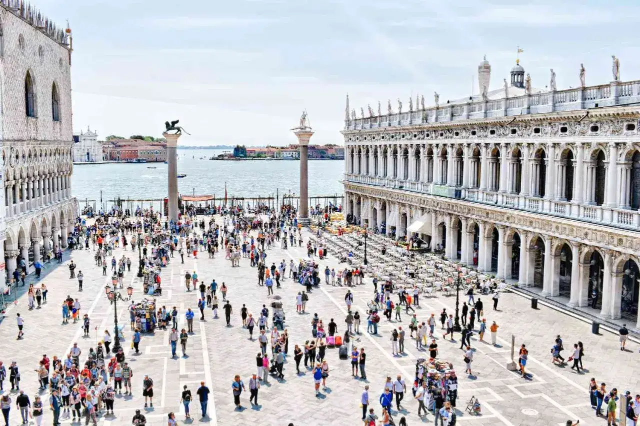 Tłum ludzi na placu San Marco w Wenecji, z widokiem na Pałac Dożów i kolumny.