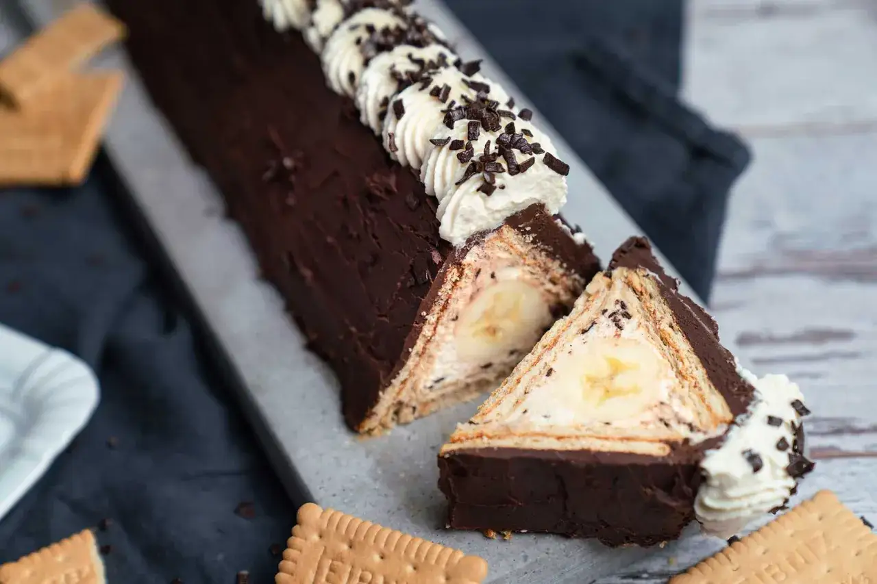 Schokoladige bananensplit torte mit Sahnetupfern und Bananenfüllung, umgeben von Keksen.