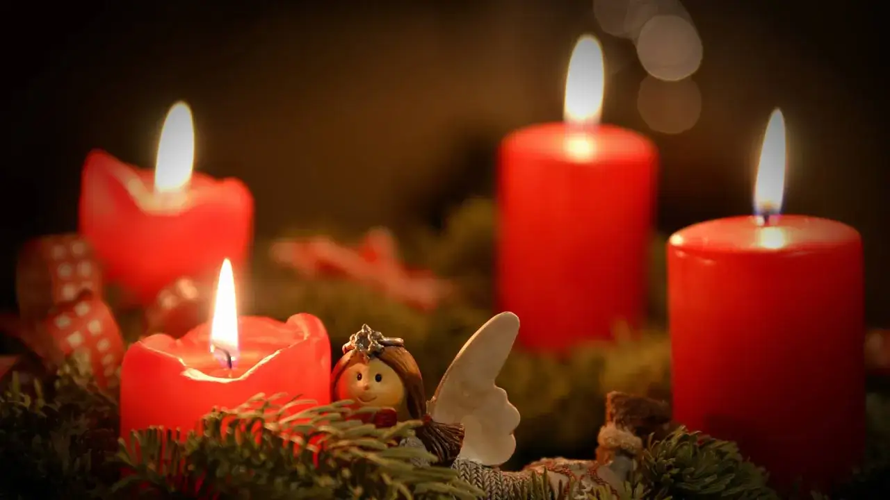 Ein Adventskranz mit vier roten Kerzen und einem kleinen Engel. Die Kerzen symbolisieren Hoffnung, Liebe, Freude und Frieden – die Adventskranz Bedeutung.