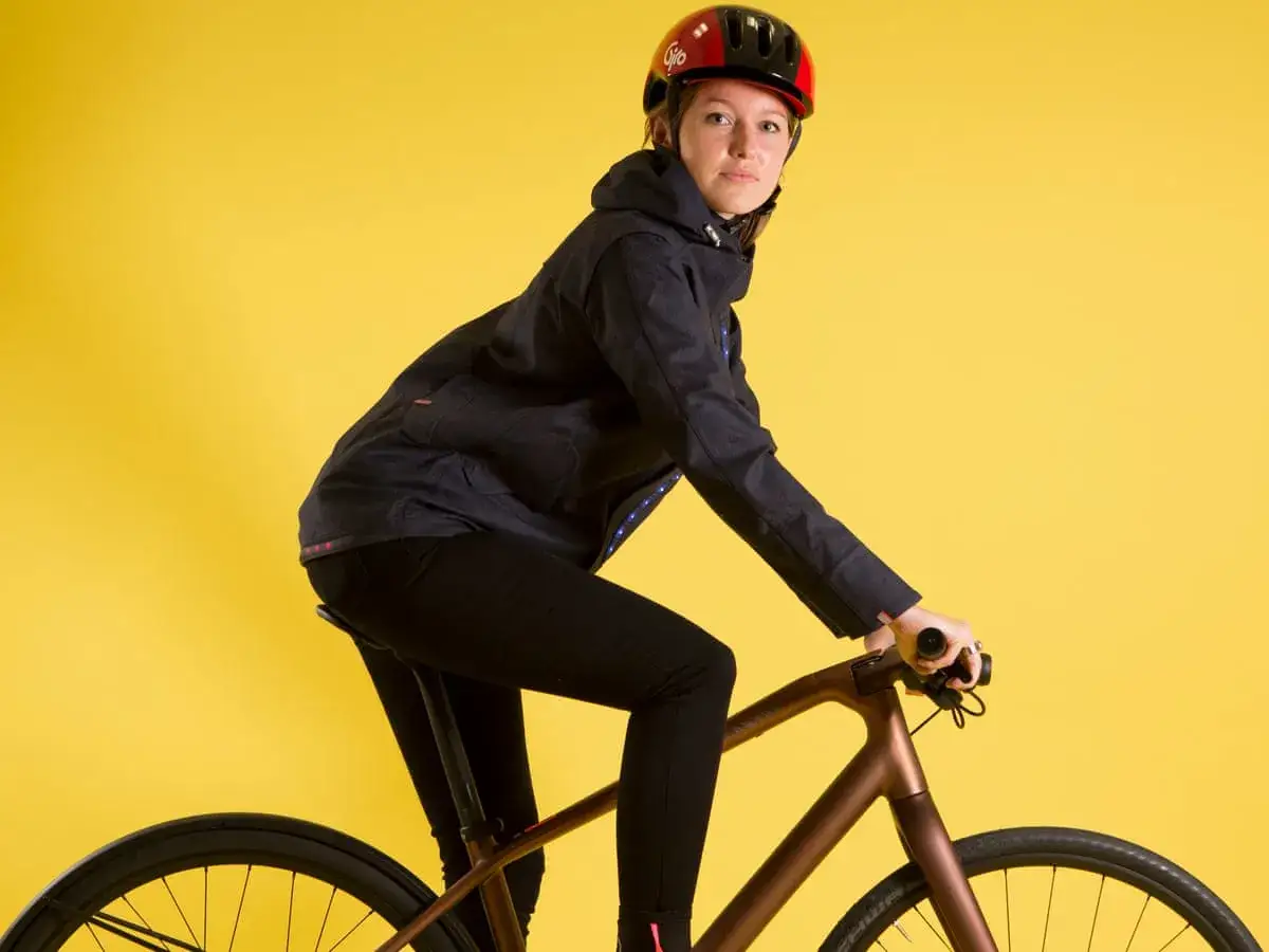 Kvinna p&aring; en modern dam cykel, kl&auml;dd i jacka och hj&auml;lm, redo f&ouml;r en tur.