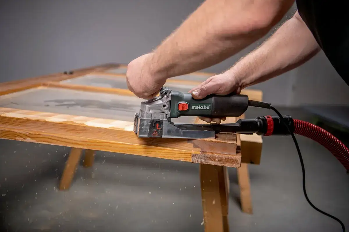 Un artisan utilise une ponceuse Metabo pour rénover une vieille porte en bois. Avis sur la marque Metabo : efficace et maniable.
