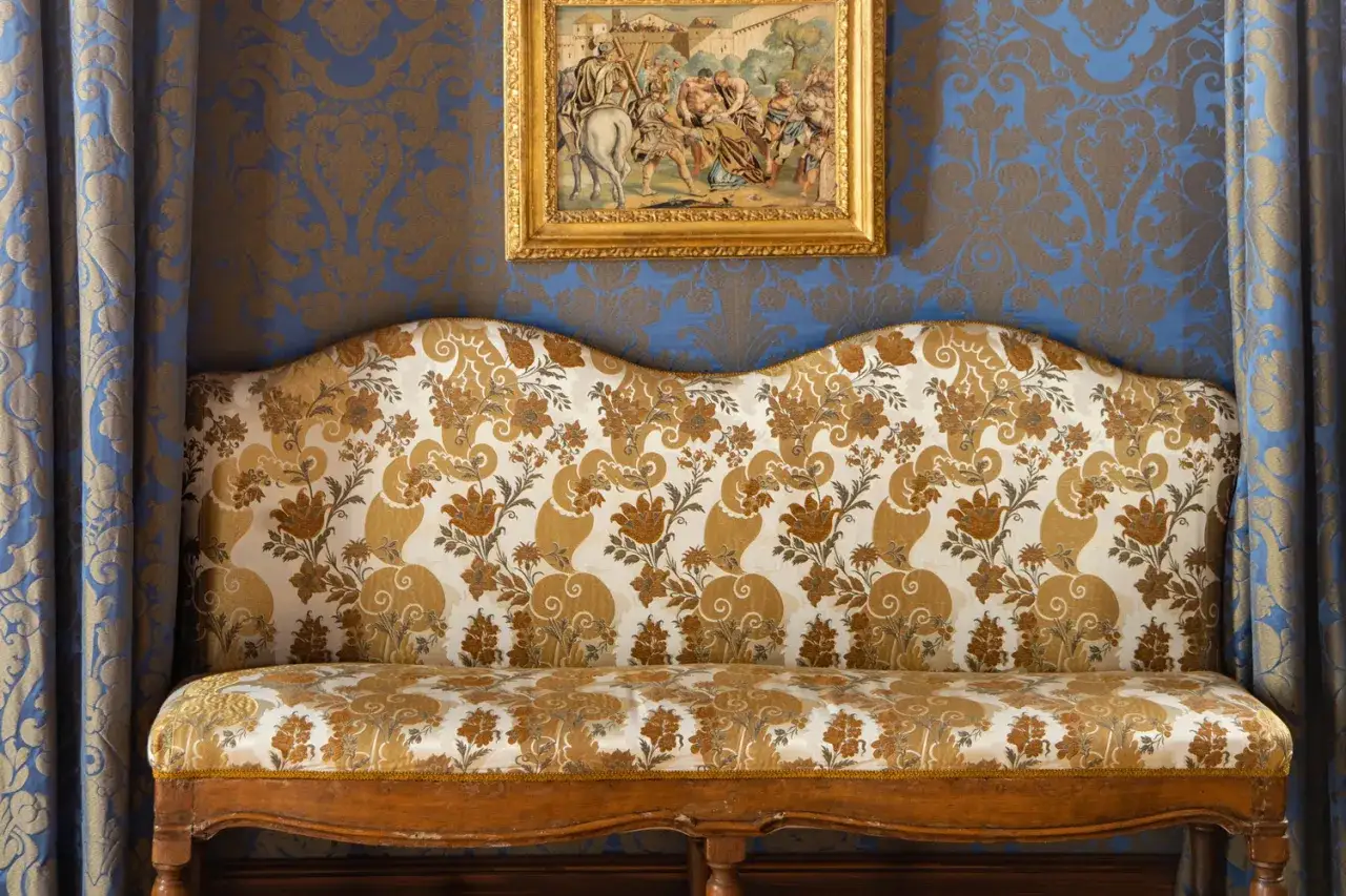 Divano con tessuto floreale dorato, tipico di un antico setificio fiorentino, su sfondo blu damascato.