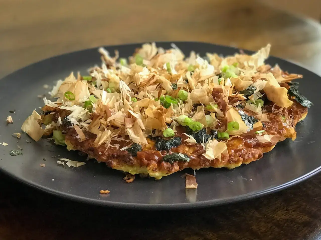 A savory okonomiyaki, a popular Japanese dish, topped with bonito flakes and green onions. This is a great example of recipes with Kewpie mayo.