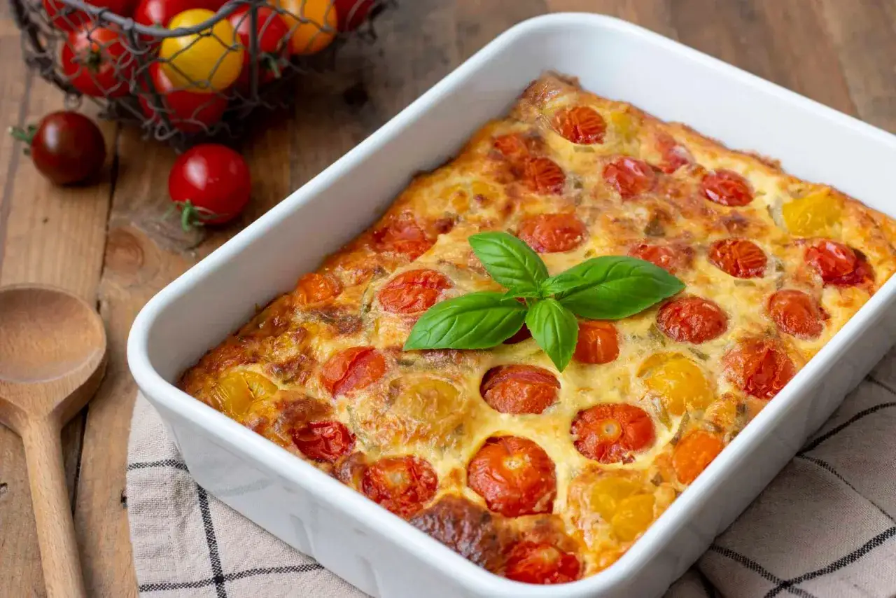 Un délicieux clafoutis tomates cerises, doré et garni de basilic frais, prêt à être dégusté.