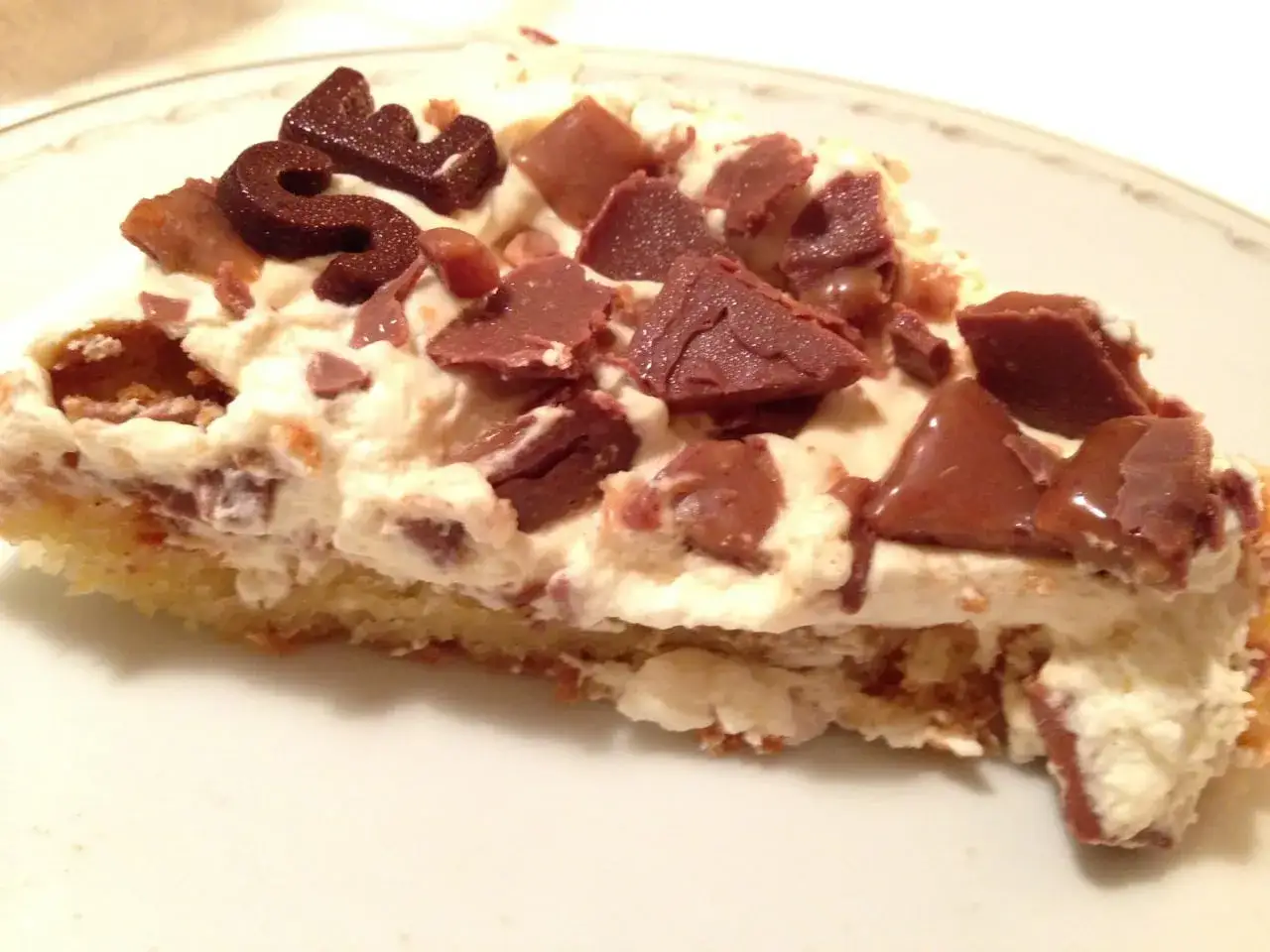 En bit krämig daim tårta med chokladbitar och en chokladdekoration.