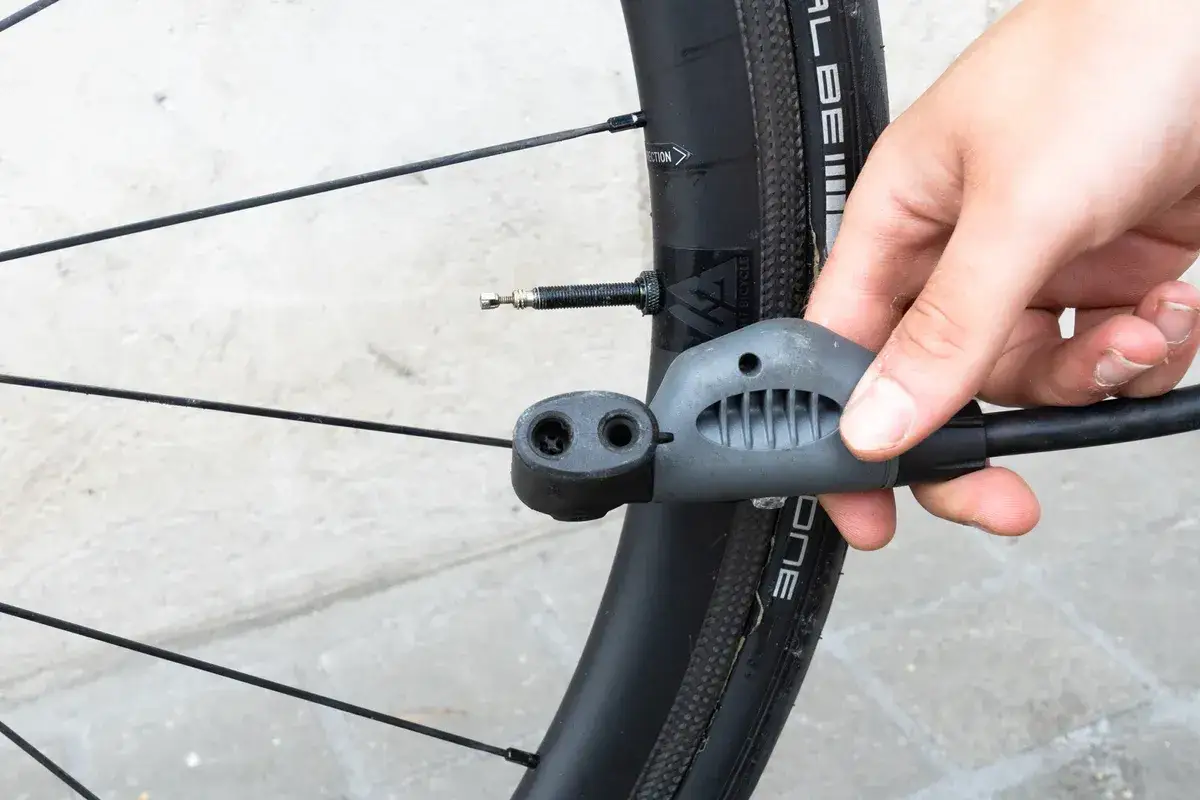 En hand håller en cykelpump mot ett cykeldäck. Enkel guide för hur pumpar man en cykel.