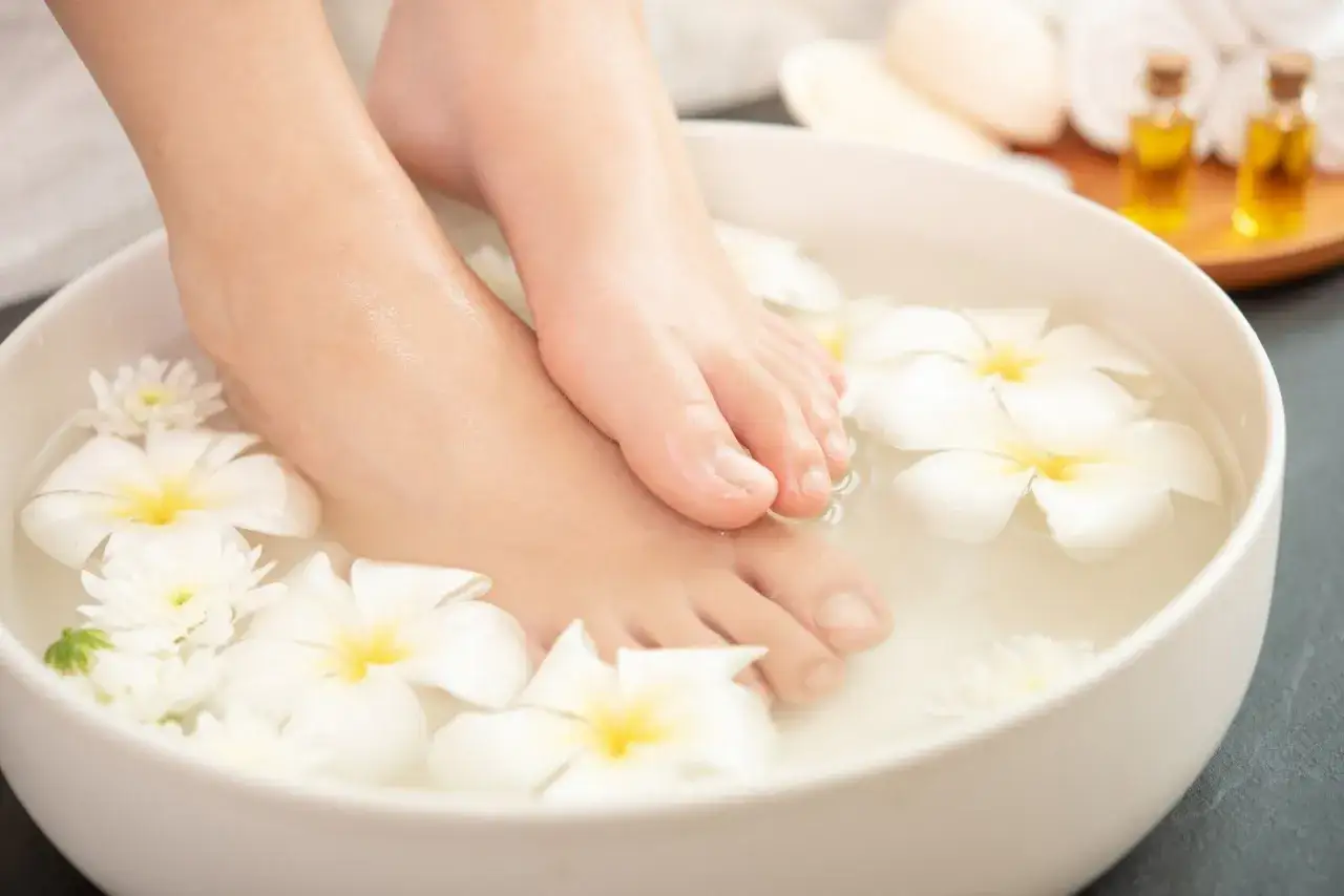 Pies sumergidos en agua con flores blancas. Un spa casero para saber como quitar el olor de los pies y relajarse.