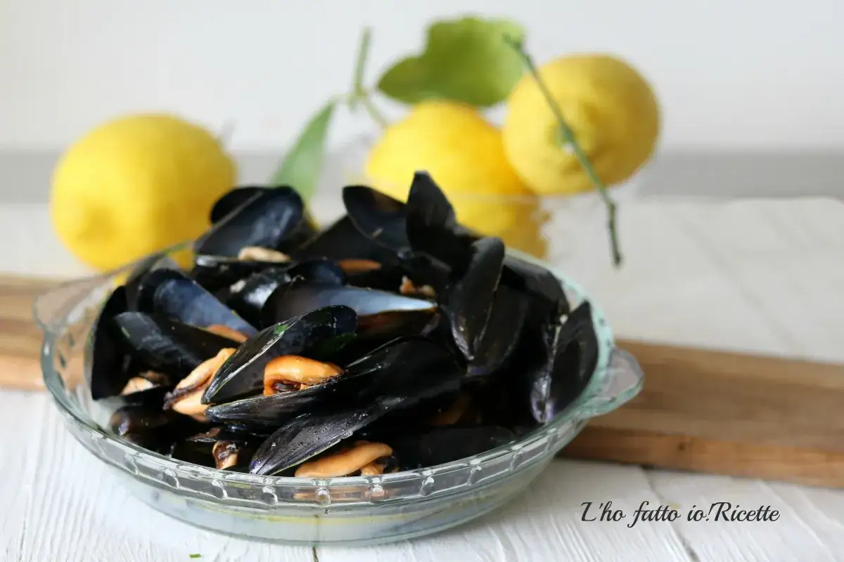 Un invitante saut&egrave; di cozze in una ciotola di vetro, con limoni freschi sullo sfondo.