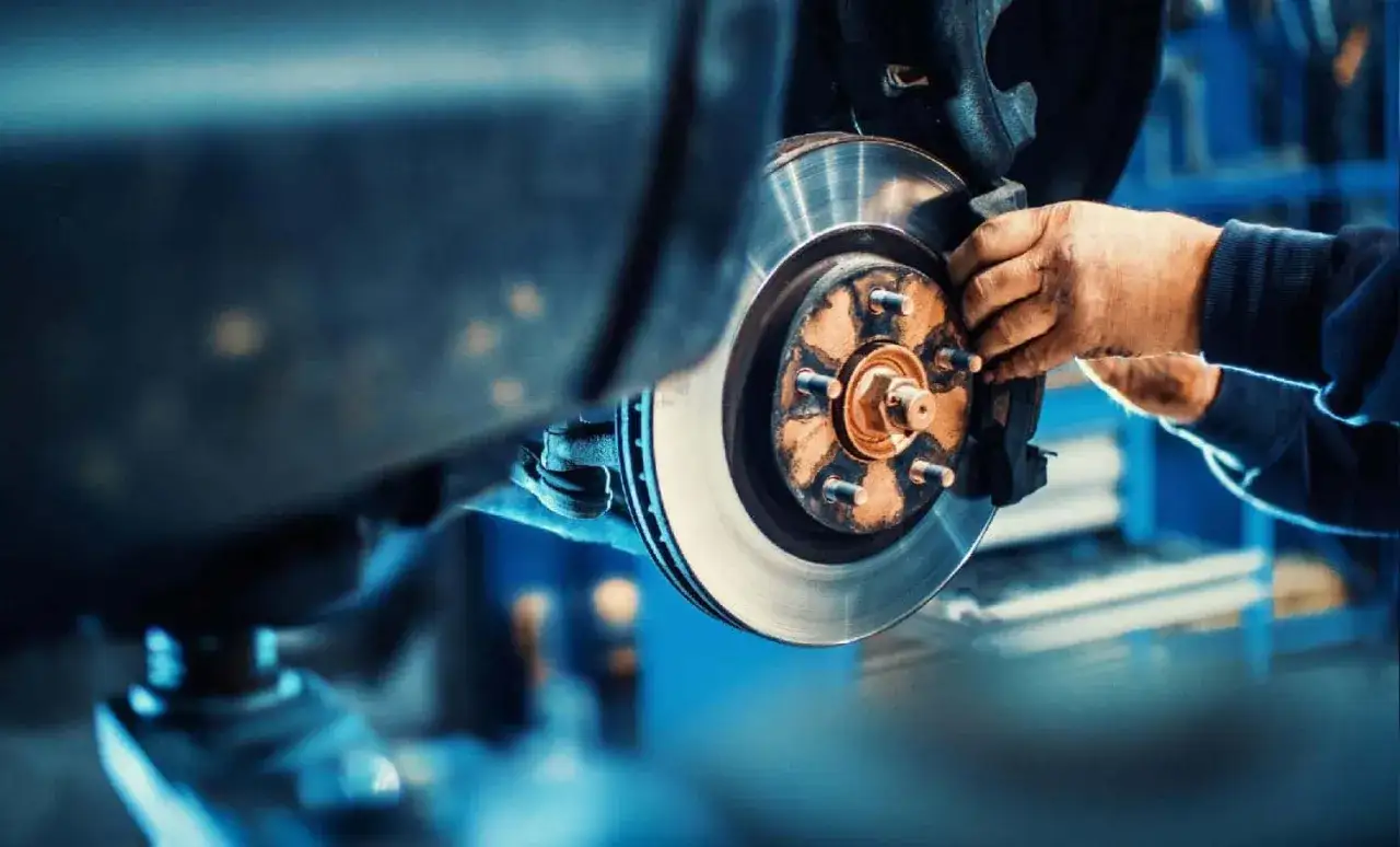 Mains d'un mécanicien en train de changer un disque de frein sur une voiture dans un atelier.