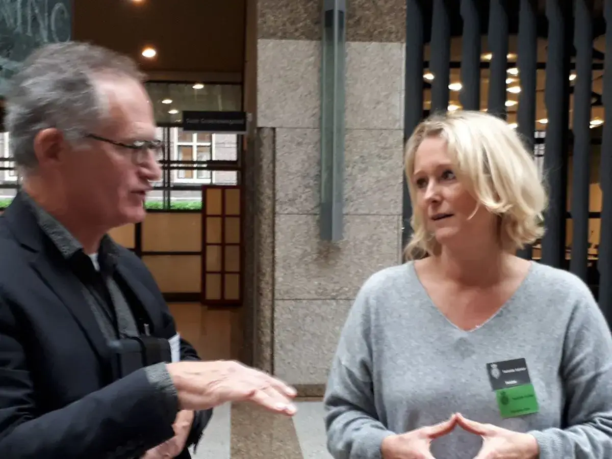 Man en vrouw in gesprek over basisinkomen Nederland. De vrouw draagt een badge met de tekst