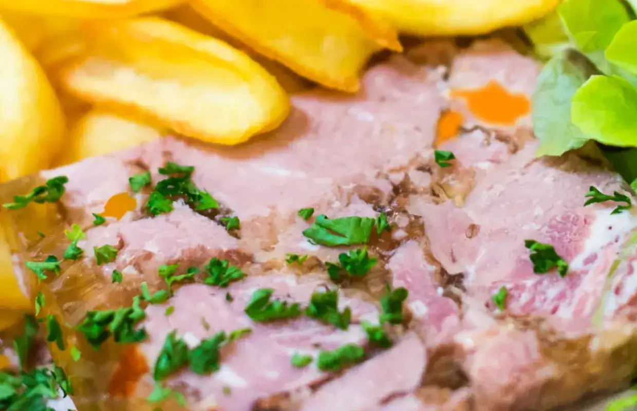 Tranche de viande blanche en gelée, garnie de persil, accompagnée de pommes de terre sautées et d'une salade verte.