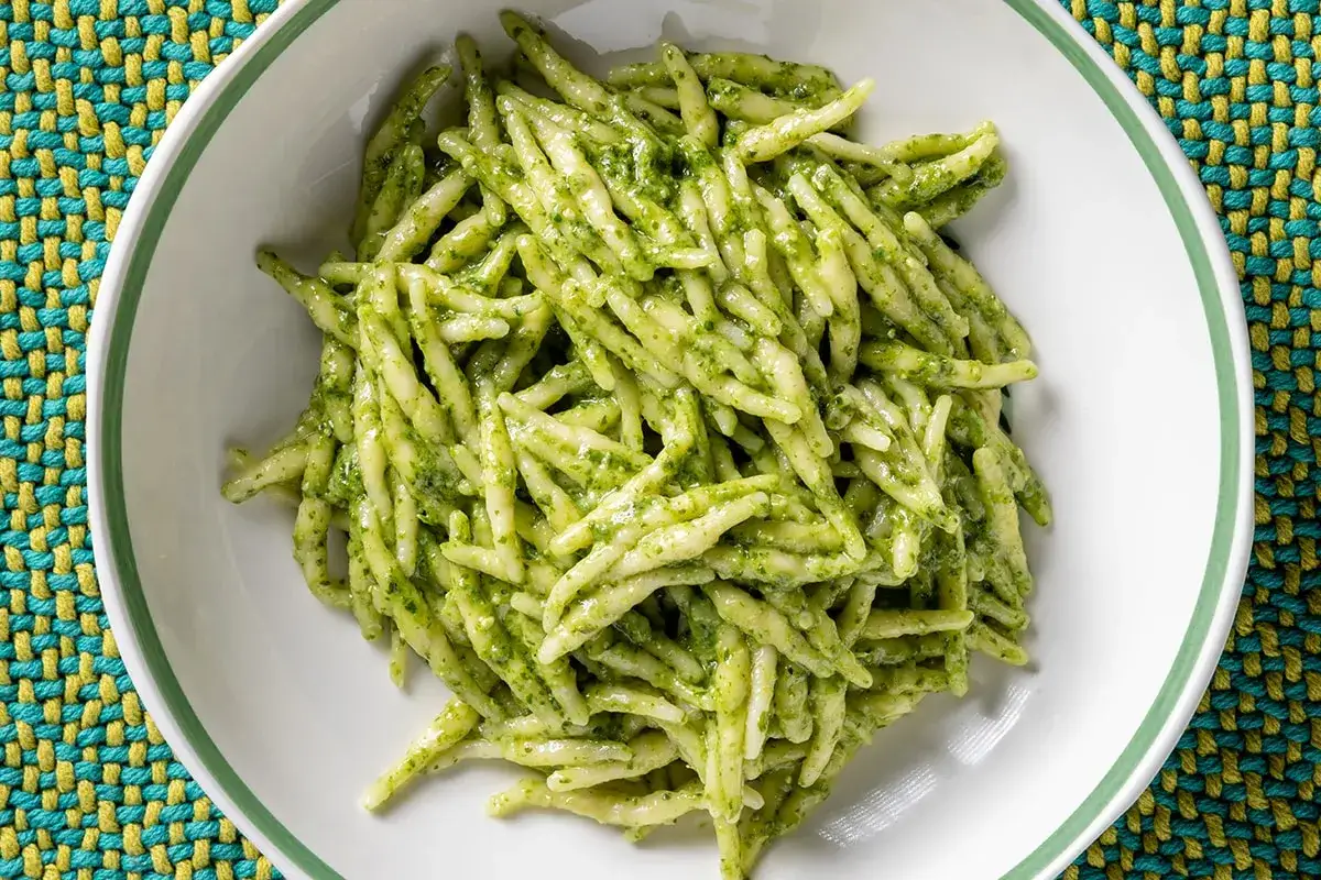 Trofie al pesto, un classico delle ricette liguri, servite in un piatto bianco su un runner colorato.