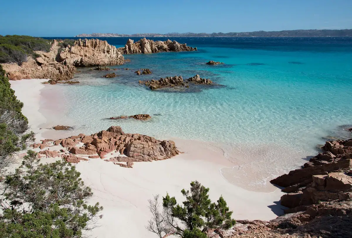 Spiaggia rosa e rocce rosse sull'isola della Maddalena, con acque cristalline turchesi e blu intenso.