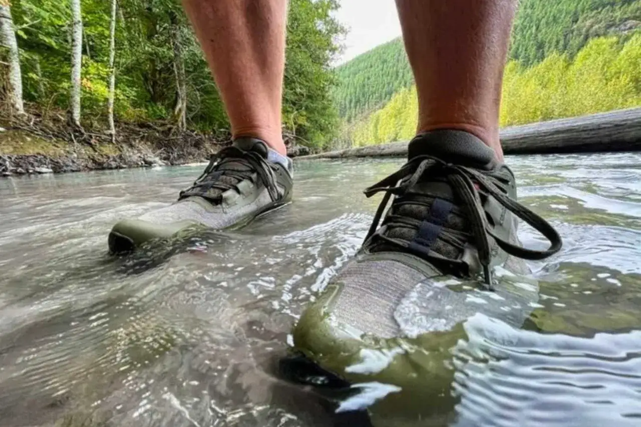 Hiking through a stream in waterproof GTX meaning shoes. The shoes are olive green with grey accents and black laces.