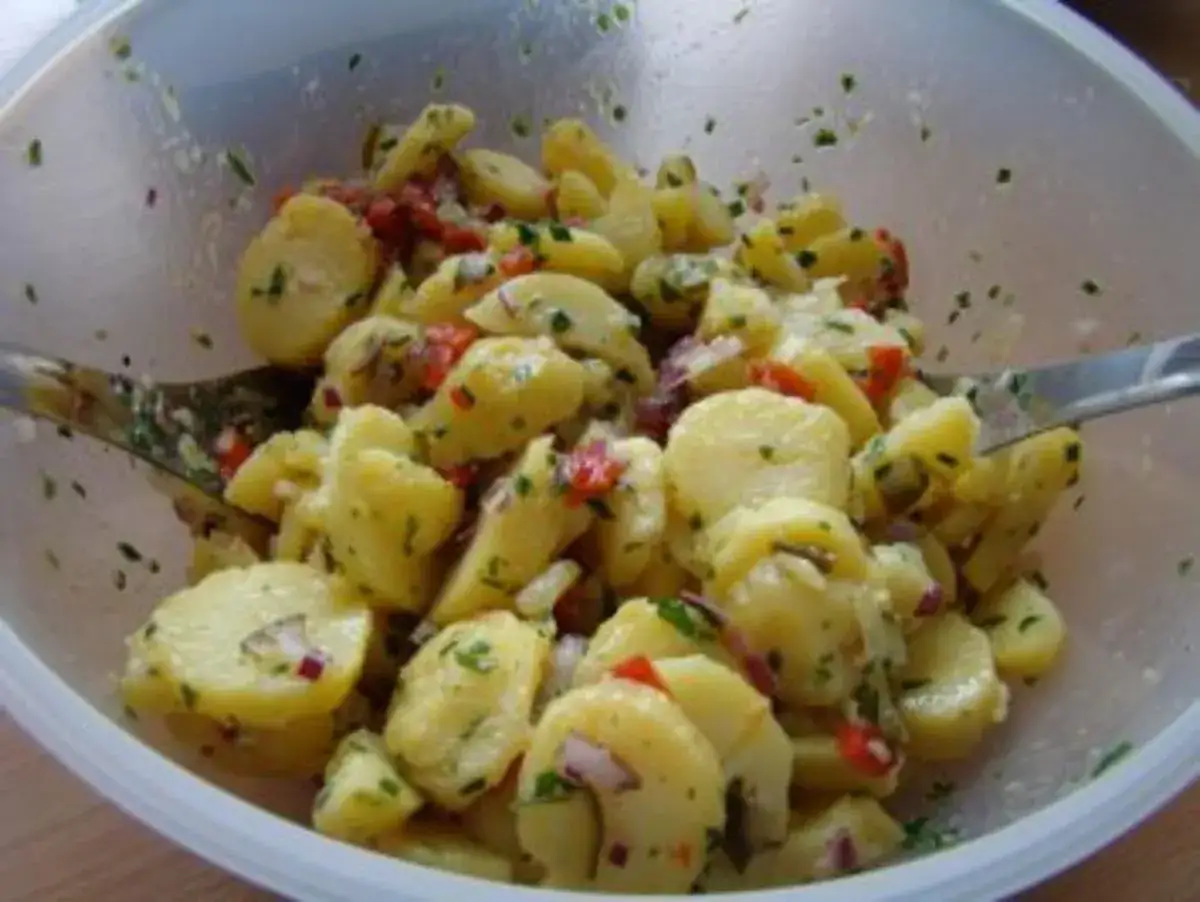 Ein köstlicher Kartoffelsalat ohne Mayo, mit frischen Kräutern und roten Zwiebeln, wird mit einer Gabel serviert.