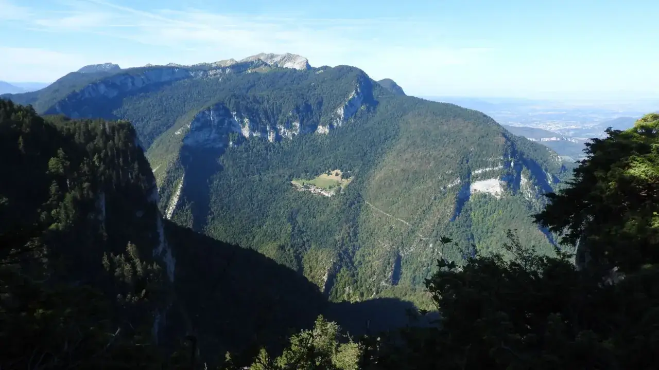 Vue panoramique sur les montagnes verdoyantes de Chartreuse, avec un hameau isol&eacute; nich&eacute; dans une clairi&egrave;re. Une rando Chartreuse insolite &agrave; explorer.