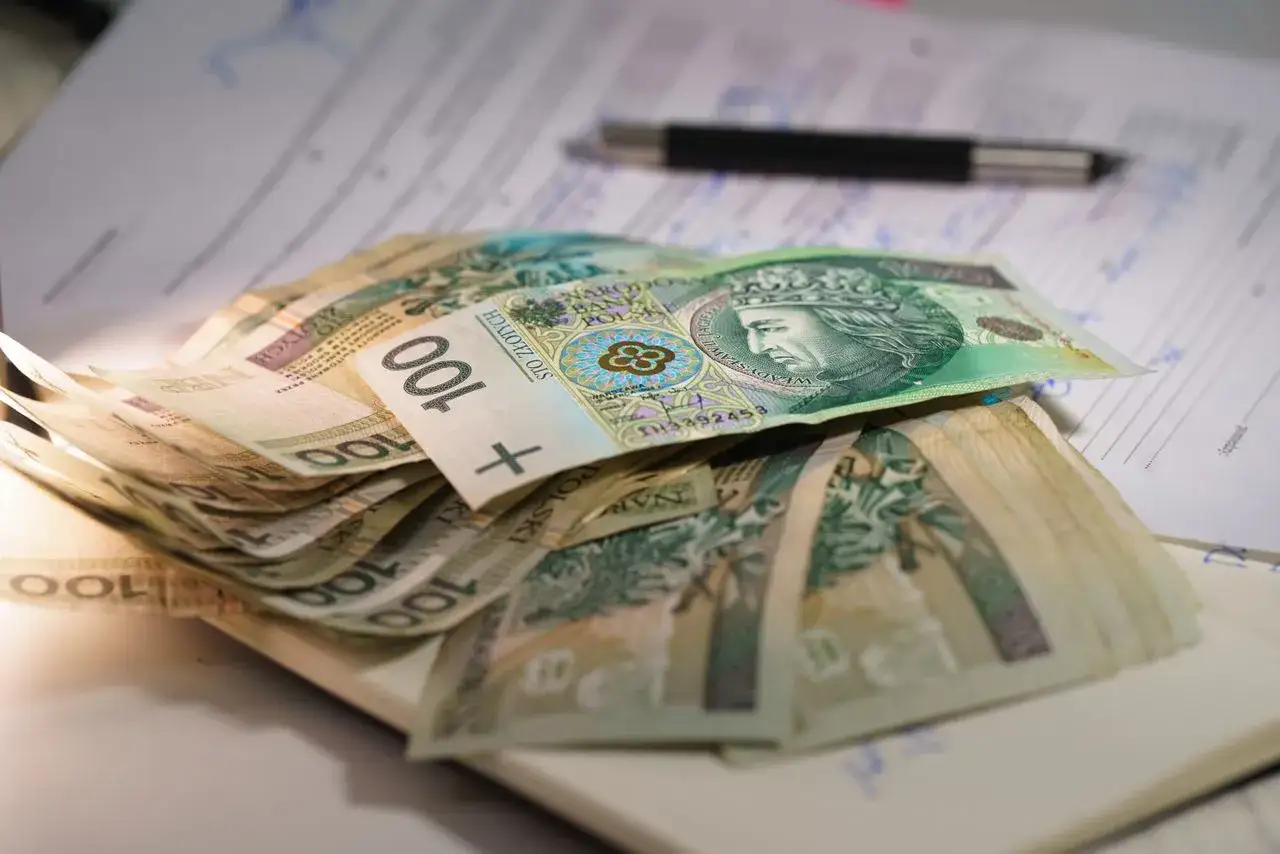 Stos banknotów 100 zł leży na dokumentach, obok długopisu. Marzenie o kredycie 50 tys. staje się bliższe.