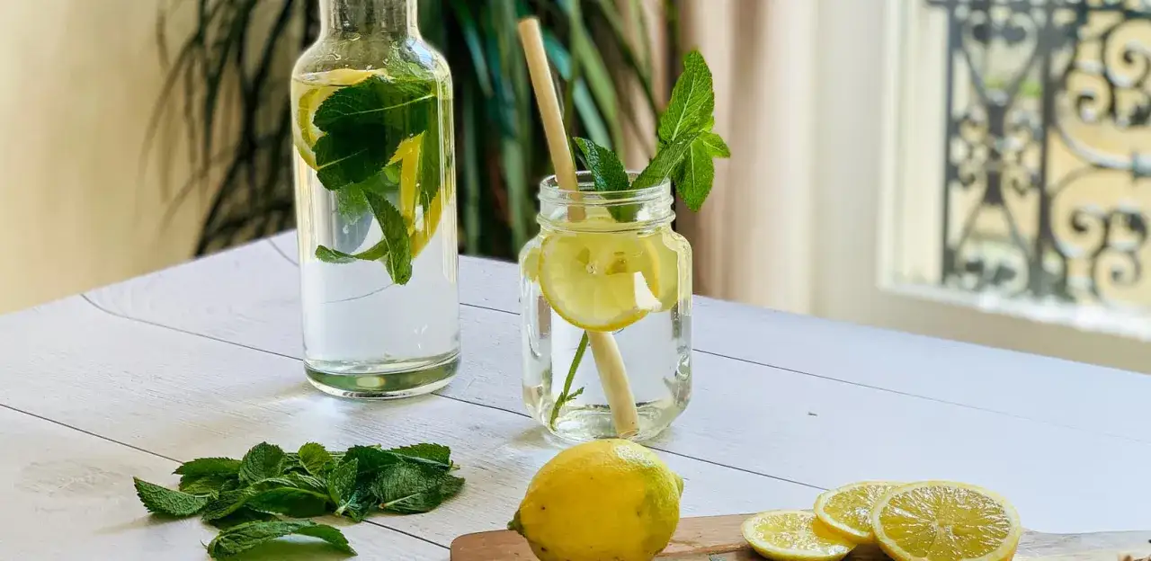 Bouteille et verre remplis de citronnade maison rafra&icirc;chissante avec des tranches de citron et des feuilles de menthe. Des citrons et de la menthe fra&icirc;che sont dispos&eacute;s sur la table.